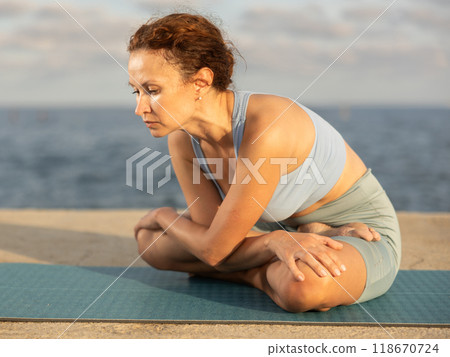 Experienced female trainer doing various exercises to warm up the body before yoga classes on seashore 118670724
