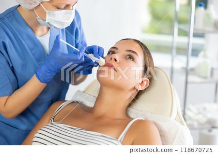Adult woman cosmetologist makes injection in lips of patient 118670725