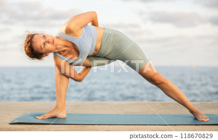 Yoga practice on embankment, female athlete fulfil carry out Parivritta Parshvakonasana 118670829