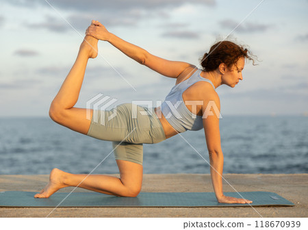 Yoga poses performed by a slender woman on seashore 118670939