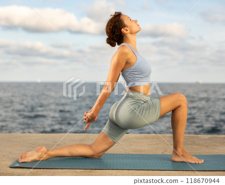 Yoga practice on embankment, female athlete fulfil carry out Anjaneyasana 118670944