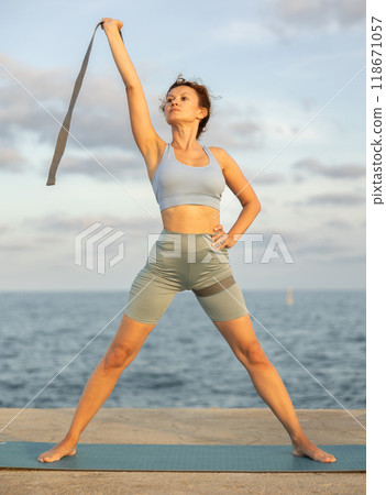 Sporty woman doing yoga with stretch band on seashore Sporty woman doing yoga with stretch band on seashore 118671057