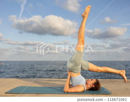 Yoga practice on embankment, female athlete fulfil carry out shoulder stand 118671061