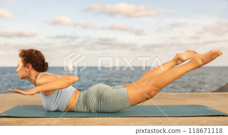 Sporty woman practicing bhujangasana yoga pose on mat on seashore Sporty woman practicing bhujangasana yoga pose on mat on seashore 118671118