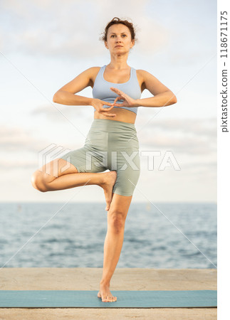 Yoga practice on embankment, female athlete fulfil carry out Vrikshasana Yoga practice on embankment, female athlete fulfil carry out Vrikshasana 118671175