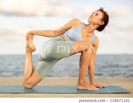 Yoga practice on embankment, female athlete fulfil carry out parivritta Anjaneyasana 118671191