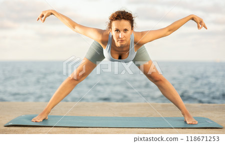 Yoga practice on embankment, female athlete fulfil carry out Prasarita Padottanasana Yoga practice on embankment, female athlete fulfil carry out Prasarita Padottanasana 118671253