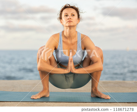 Woman practicing yoga on sea beach, stretching in an asymmetrical seated asana Parivritta Janu Sirsasana 118671278