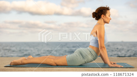 Yoga practice on embankment, female athlete fulfil carry out Urdhva Mukha Shvanasana 118671324