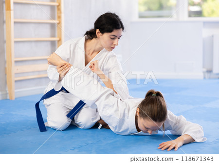 Sportive woman holds her opponent by force while sitting on mats during judo classes Sportive woman holds her opponent by force while sitting on mats during judo classes 118671343