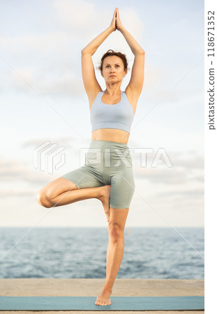Athletic female yoga practitioner performing Garudasana on beach Athletic female yoga practitioner performing Garudasana on beach 118671352