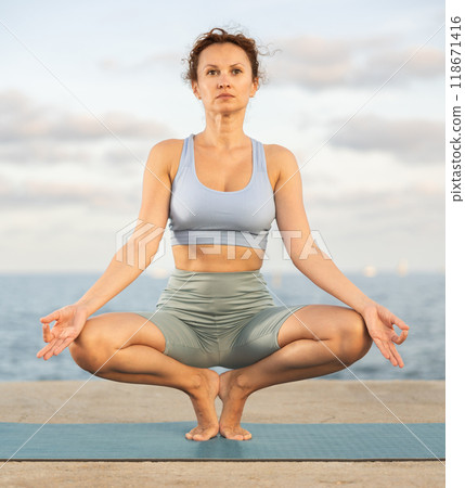 Woman practicing yoga on sea beach, stretching in an asymmetrical seated asana Parivritta Janu Sirsasana Woman practicing yoga on sea beach, stretching in an asymmetrical seated asana Parivritta Janu Sirsasana 118671416