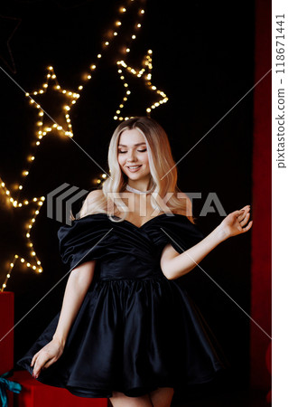 Blonde woman in black dress posing for photo in front of Christmas tree 118671441