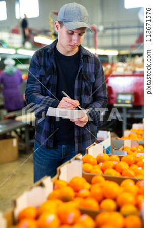 Positive male worker fills out a document at a citrus processing plant. 118671576