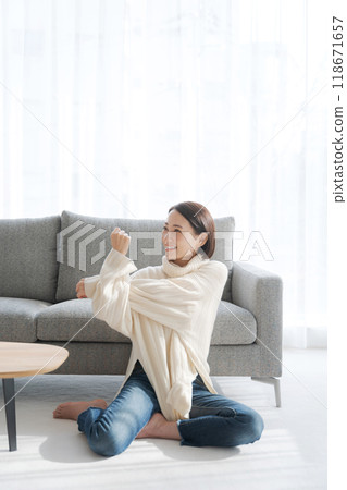 Young woman stretching while sitting on the floor in the living room 118671657