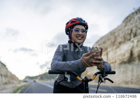 cheerful woman riding bike using phone 118672486