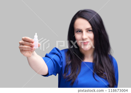 Woman in blue shirt holding eye drops against gray background, promoting eye 118673004