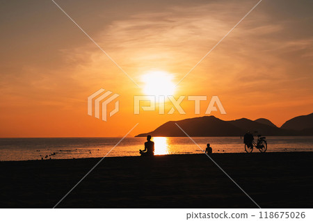 silhouette of a man sitting and meditating on the beach by the sea in evening at sunset in summer 118675026