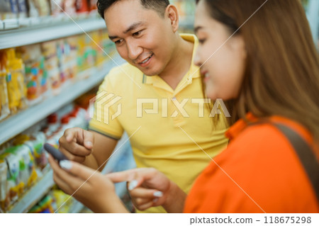 Asian man pointing mobile phone shown by young woman in supermarket Asian man pointing mobile phone shown by young woman in supermarket 118675298