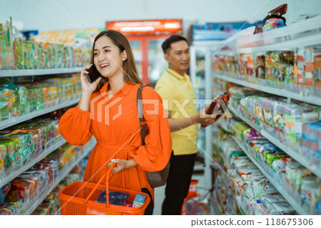 Asian woman carrying cart while making a call with mobile phone Asian woman carrying cart while making a call with mobile phone 118675306