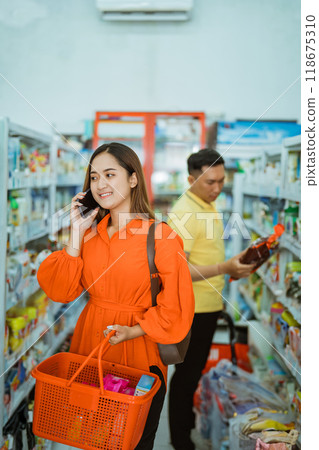 beautiful woman carrying cart while calling on background of man shopping beautiful woman carrying cart while calling on background of man shopping 118675310