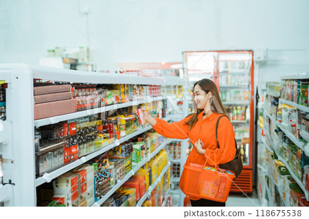 young woman picking up items on a shelf with a red cart 118675538
