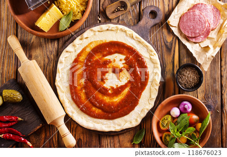 Raw pizza dough with tomato sauce and basil leaves. Raw pizza dough with tomato sauce and basil leaves. 118676023
