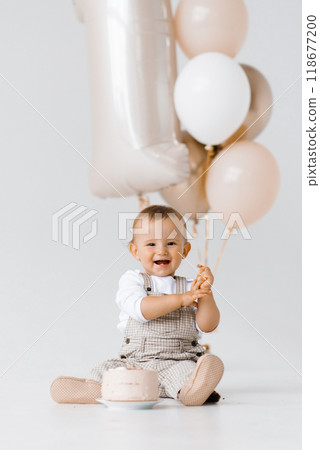 Happy laughing baby boy is sitting next to a birthday cake and balloons Happy laughing baby boy is sitting next to a birthday cake and balloons 118677200