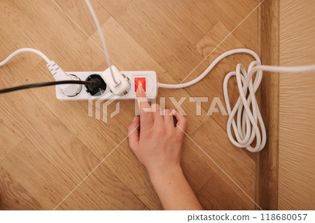 Top view of female hand turn on the extension cord at home. White cable connector 118680057