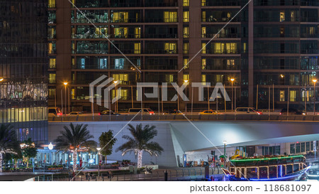 Yachts and boats with tourists staying near shoping mall and passing under a bridge in Dubai Marina district night timelapse. 118681097