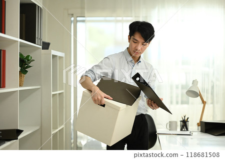 Disappointed male office worker packing his belongings into a cardboard box after being fired Disappointed male office worker packing his belongings into a cardboard box after being fired 118681508