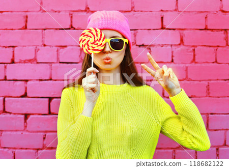 Colorful portrait stylish modern teenage girl with lollipop, vivid yellow sweater, glasses, pink hat 118682122