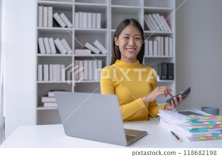 woman meticulously plans a finance audit, using a computer and calculator to review budget documents and ensure accuracy 118682198