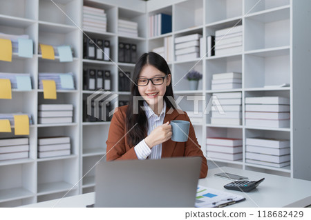 A businesswoman takes a break from her financial tasks, relaxing with a cup of coffee to recharge before continuing her work. A businesswoman takes a break from her financial tasks, relaxing with a cup of coffee to recharge before continuing her work. 118682429