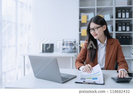 woman meticulously plans a finance audit, using a computer and calculator to review budget documents and ensure accuracy 118682432