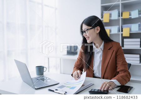woman meticulously plans a finance audit, using a computer and calculator to review budget documents and ensure accuracy 118682433