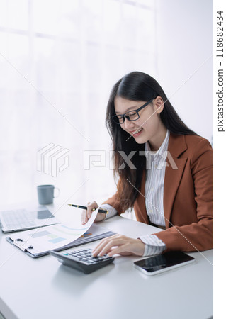 woman meticulously plans a finance audit, using a computer and calculator to review budget documents and ensure accuracy 118682434