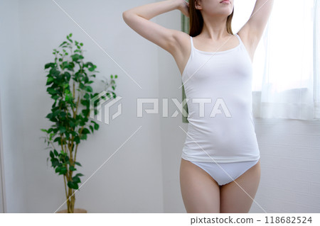 年輕苗條的女子穿著漂亮的內衣，舒展著背部，沐浴在早晨的陽光下。 118682524