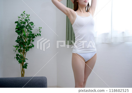 年輕苗條的女子穿著漂亮的內衣,舒展著背部,沐浴在早晨的陽光下。 年輕苗條的女子穿著漂亮的內衣,舒展著背部,沐浴在早晨的陽光下。 118682525