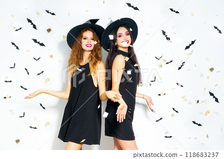 portrait of two happy young women in black witch halloween costumes. firecrackers in the background. portrait of two happy young women in black witch halloween costumes. firecrackers in the background. 118683237