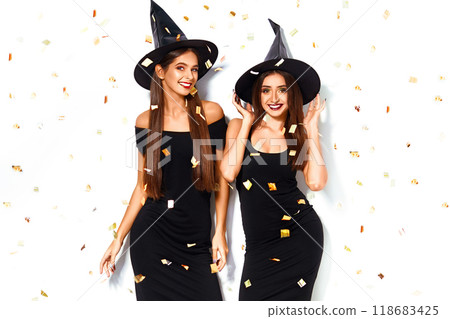 nice portrait of two beautiful young woman in black witch halloween costumes on party over white background. 118683425