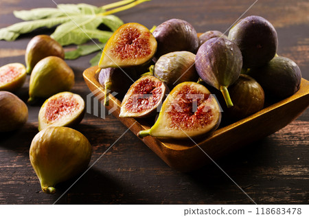 A close-up photo of fresh figs, some whole and some halved, displayed in a wooden bowl A close-up photo of fresh figs, some whole and some halved, displayed in a wooden bowl 118683478