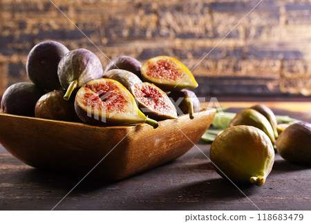 A close-up photo of fresh figs, some whole and some halved, displayed in a wooden bowl 118683479