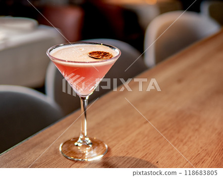 Red cocktail in martini glass on bar counter in restaurant interior. Gin alcohol cocktail decorated egg white and dry lichee fruit slice. Pink cold alcoholic cocktail in bar or nightclub background 118683805