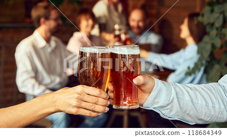 Close-up cheers, while blur of friends behind celebrate with raised glasses. Scene set for a great game day with friends and beer. Close-up cheers, while blur of friends behind celebrate with raised glasses. Scene set for a great game day with friends and beer. 118684349