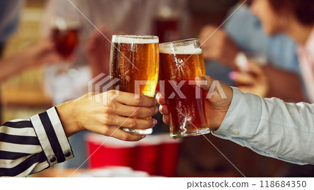 Couple of fans clink their glasses, surrounded by warm, blurred scene of sports lovers and friends. Excitement and tension of game build up. Couple of fans clink their glasses, surrounded by warm, blurred scene of sports lovers and friends. Excitement and tension of game build up. 118684350