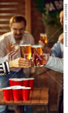 Focused on toast, while blurred figures behind cheer and engage, perfect scene of friends celebrating their team's victory with cold drinks. Focused on toast, while blurred figures behind cheer and engage, perfect scene of friends celebrating their team's victory with cold drinks. 118684366