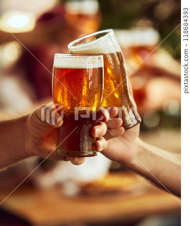 Two hands clink glasses and foam spilling over. Blurred cheering fans in background elevate celebratory spirit. Selective focus. 118684393