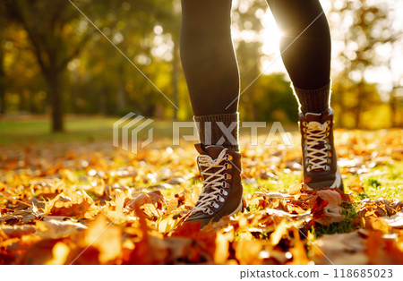 Close-up of feet in hiking boots in clearing among fallen leaves in sunny autumn park. outdoor walk. 118685023