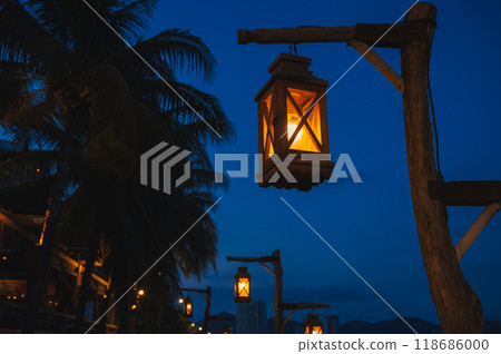 An old street lamp on a lamppost illuminating a dark street with palm trees An old street lamp on a lamppost illuminating a dark street with palm trees 118686000